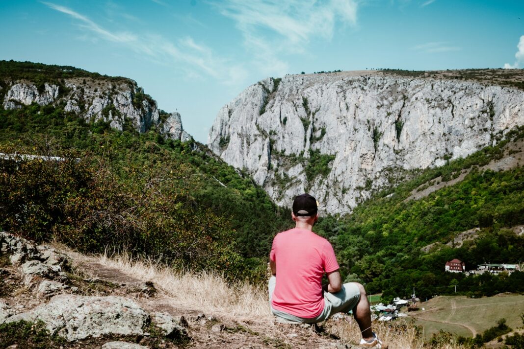 A man sitting on top of a hill next to a lush green hillside